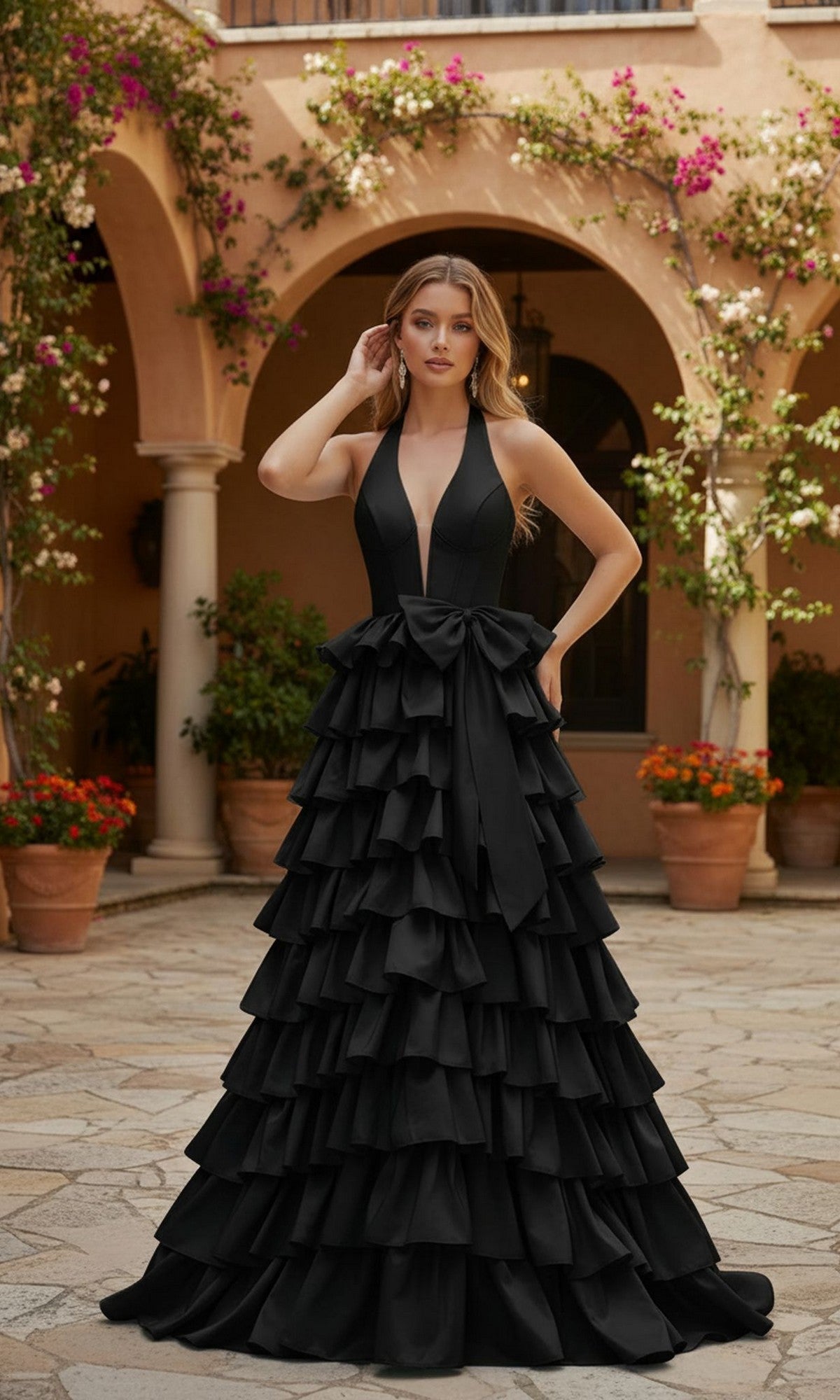 A woman stands outdoors in front of a building, wearing the PromGirl Exclusive 250045 Halter Prom Ball Gown in black, featuring a sleeveless design, tiered ruffle skirt, and a large bow at the waist.